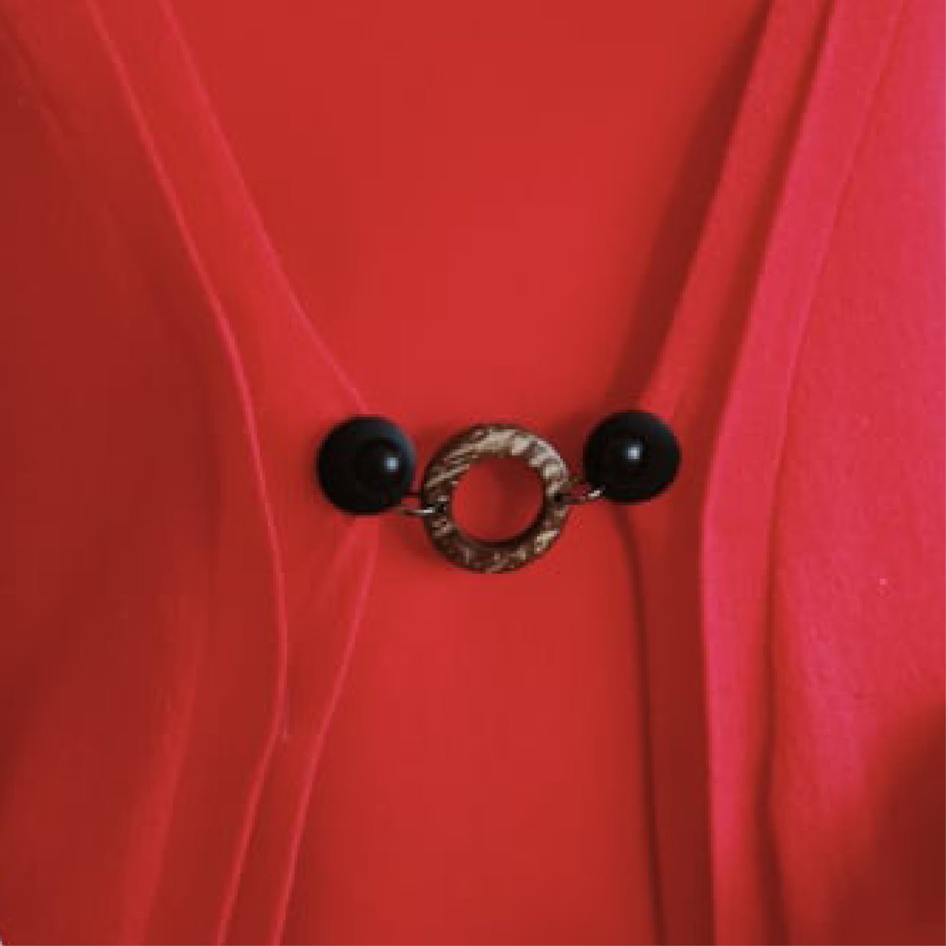 Vestsluiting Kokos zwart in close-up op een rood vest, stijlvolle Fashionclip met zwarte clips en natuurlijke ringvormige tussenbedel.