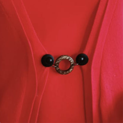 Vestsluiting Kokos zwart in close-up op een rood vest, stijlvolle Fashionclip met zwarte clips en natuurlijke ringvormige tussenbedel.