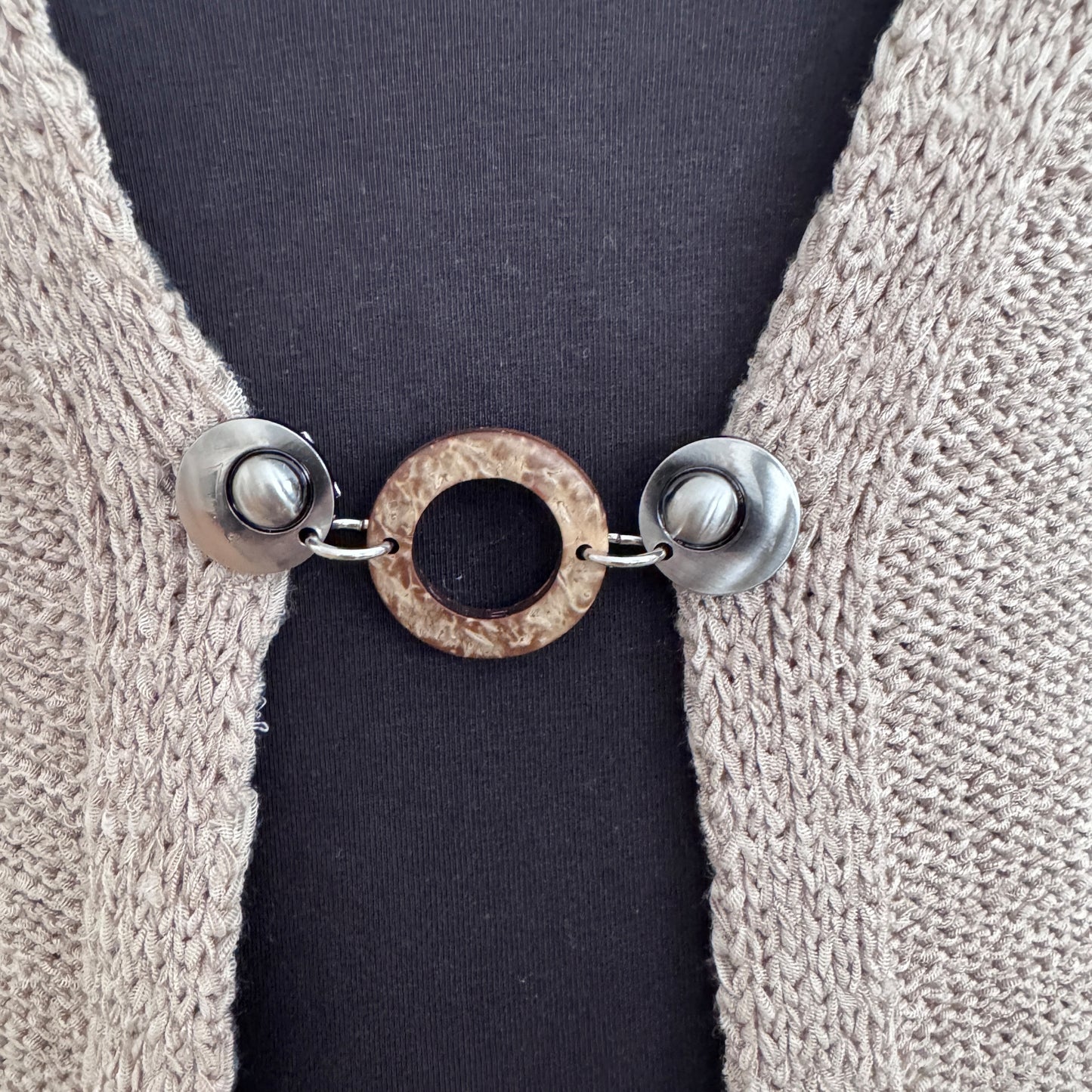 Vestsluiting Kokosnoot zilver in close-up op een gebreid vest, elegante Fashionclip met zilverkleurige clips en natuurlijke kokosring.