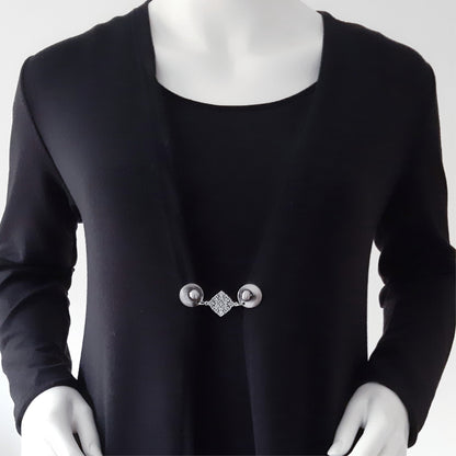 Vestsluiting met zilverkleurige clips en sierlijke ruitvormige tussenbedel, elegante Fashionclip gedragen op een zwart vest.