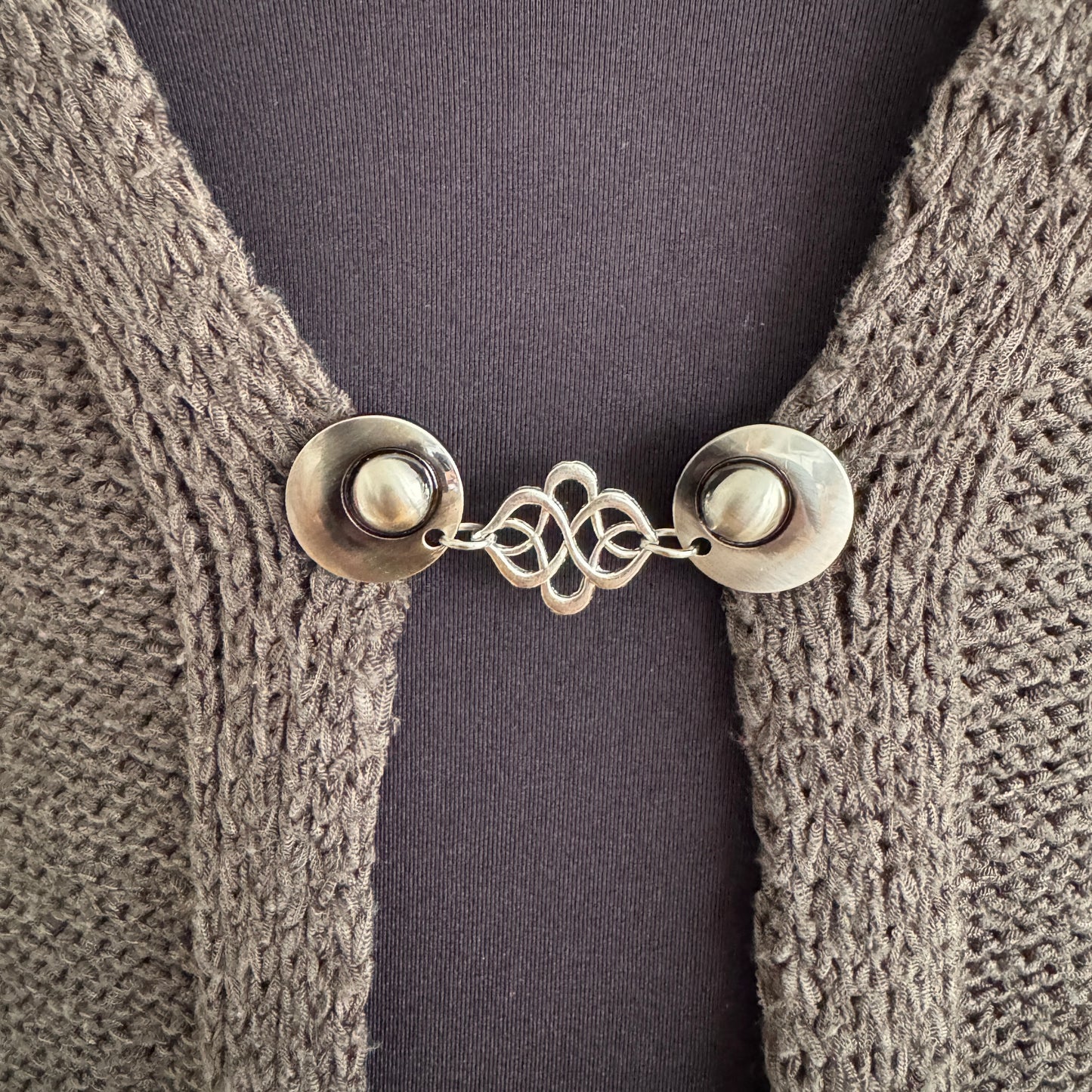 Vestsluiting Verbinding in close-up op een gebreid vest, elegante Fashionclip met zilverkleurige clips en sierlijke verbindende tussenbedel.