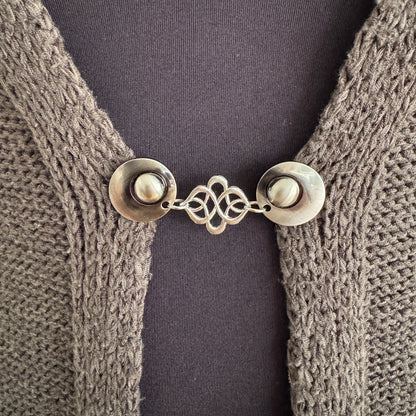 Vestsluiting Verbinding in close-up op een gebreid vest, elegante Fashionclip met zilverkleurige clips en sierlijke verbindende tussenbedel.