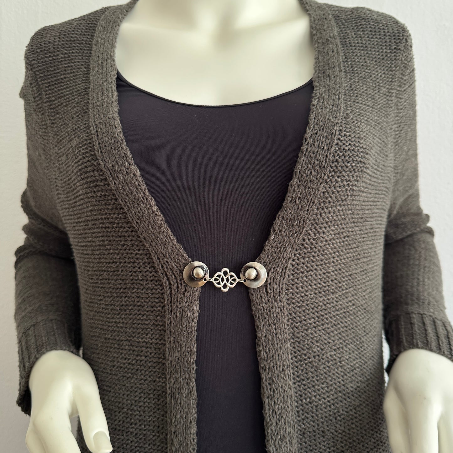 Vestsluiting Verbinding gedragen op een donker gebreid vest, elegante Fashionclip met zilverkleurige clips en sierlijke verbindende tussenbedel.
