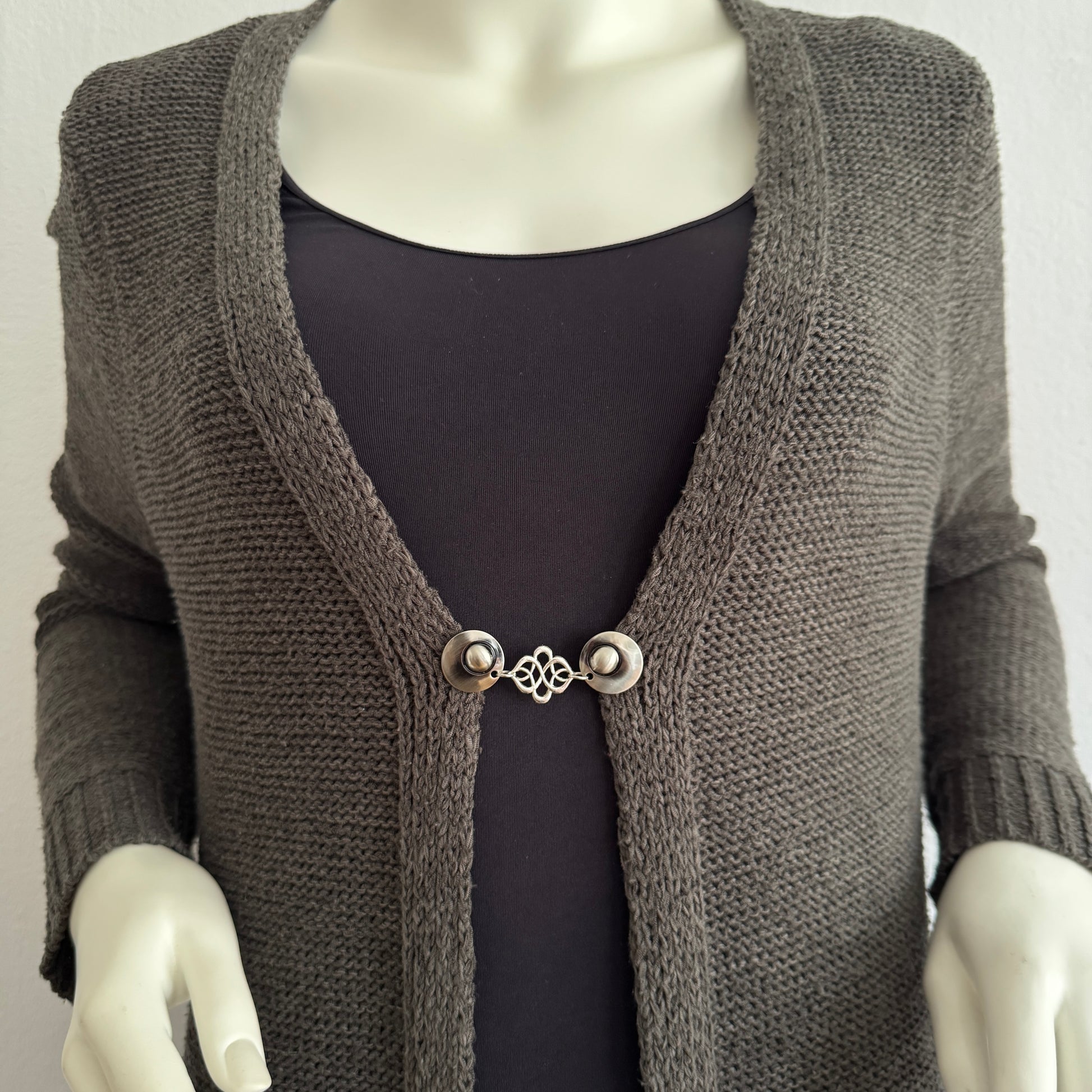 Vestsluiting Verbinding gedragen op een donker gebreid vest, elegante Fashionclip met zilverkleurige clips en sierlijke verbindende tussenbedel.