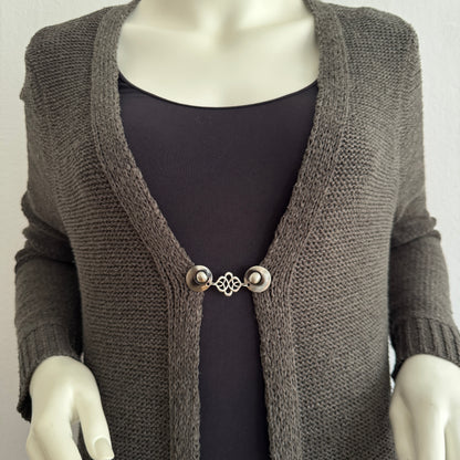 Vestsluiting Verbinding gedragen op een donker gebreid vest, elegante Fashionclip met zilverkleurige clips en sierlijke verbindende tussenbedel.
