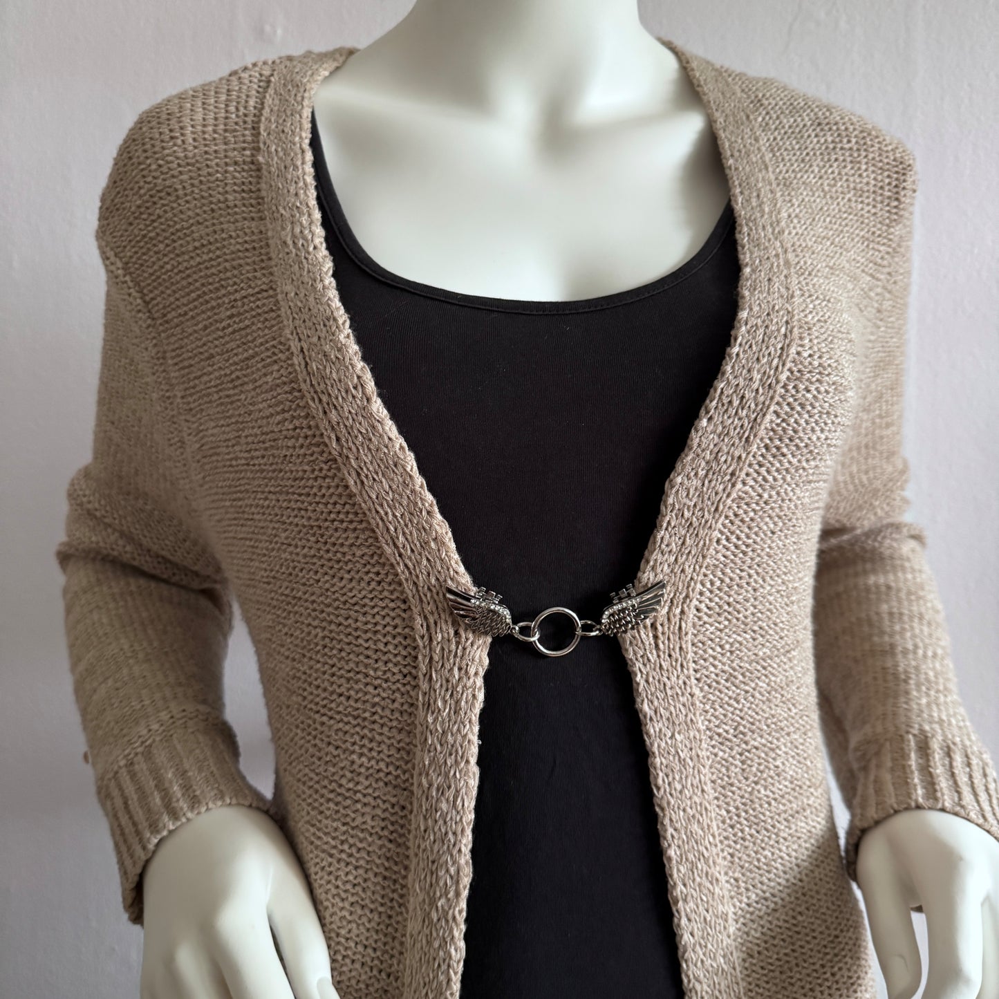 Vestsluiting Vleugels van Vrijheid zilver gedragen op een beige gebreid vest, elegante Fashionclip met vleugelvormige clips en ronde ringverbinding.