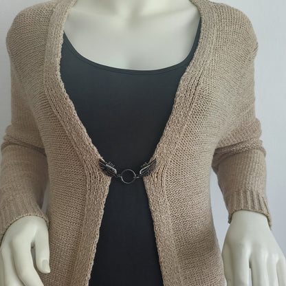 Zwarte glanzende vestsluiting met gedetailleerde vleugels en ronde ring, elegant bevestigd aan een beige vest.